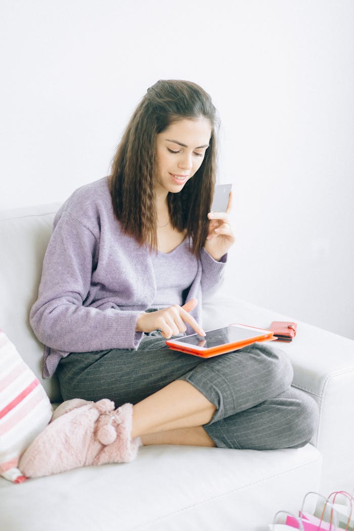 Young woman using a tablet and credit card for online shopping while sitting comfortably at home.