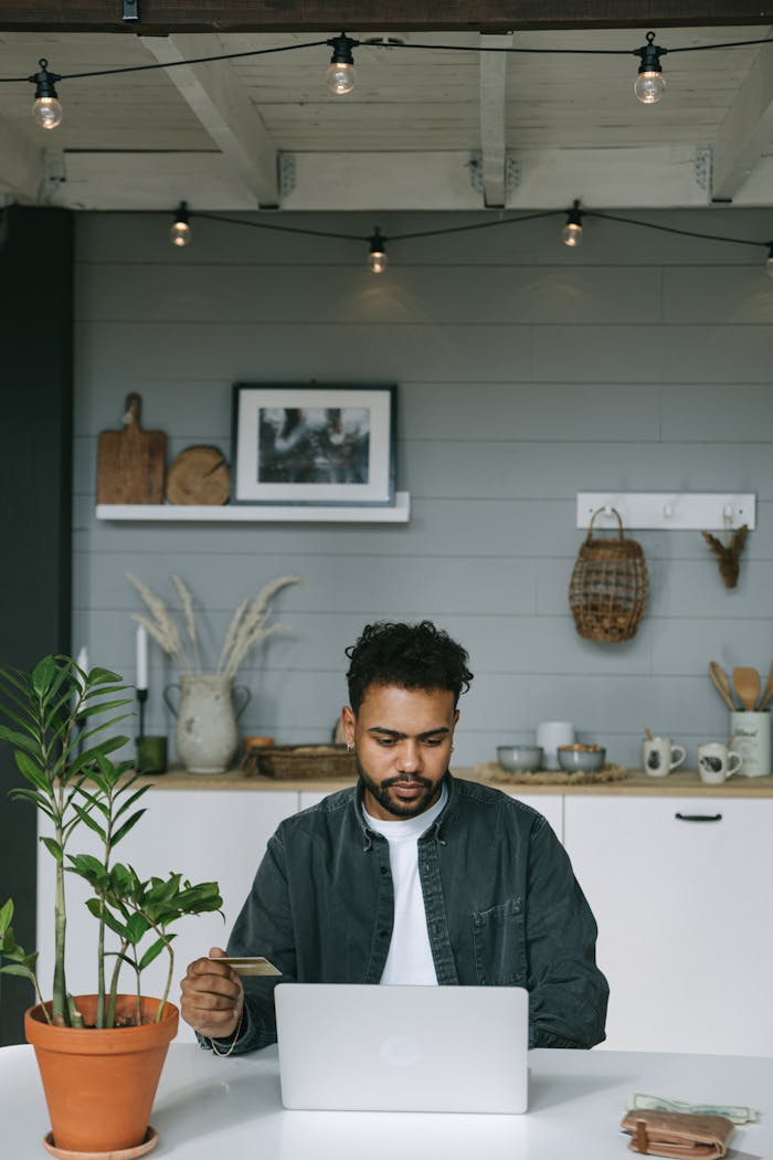 A man using a laptop and credit card for online shopping in a cozy indoor setting.